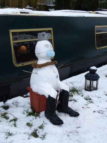 Canalside snowman A snowman sitting beside a canal boat, with black boots, a flowerpot hat and a disposable mask.
