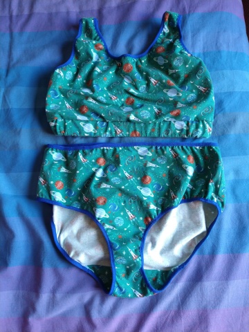 a crop-top bra and matching pants in teal fabric with a print of old-fashioned space rockets and planets, with royal blue elastic trim