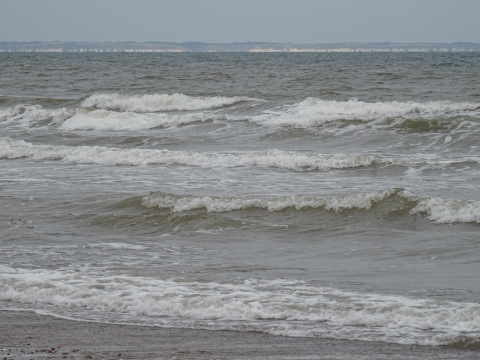 Grey sea White breakers in a grey sea with white cliffs visible in the distance.