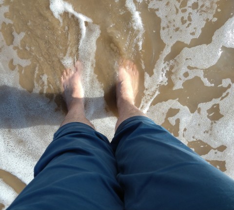Paddling A pair of white feet and legs in blue trousers standing in foaming seawater.