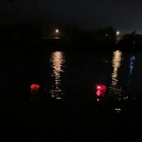 A dark lake, with two streetlamps on the far side reflected in the water, and two glowing orange floats in the water.